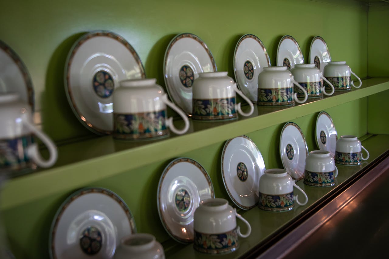Elegant rows of decorative cups and saucers arranged on a green shelf indoors.